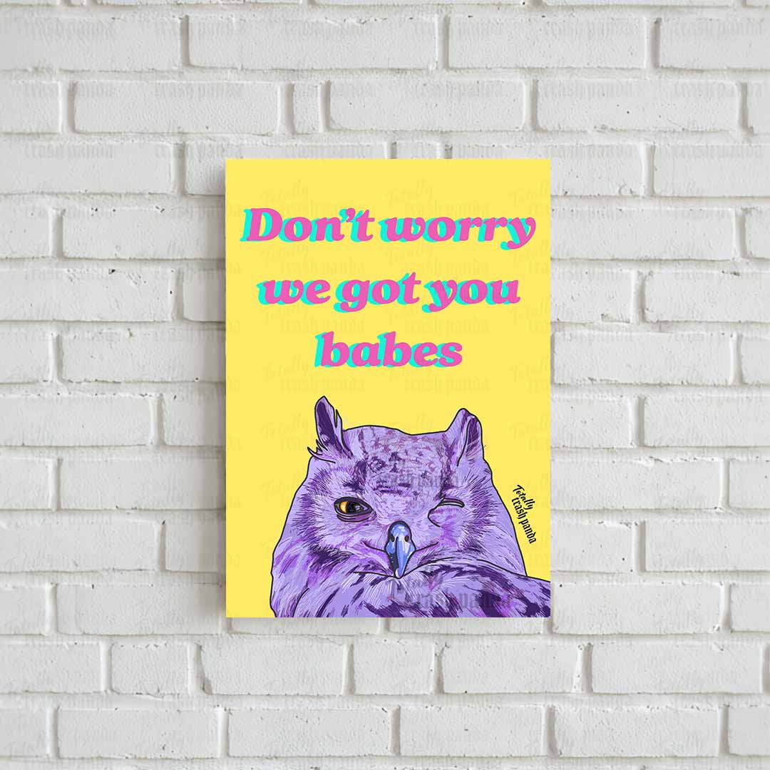 A vertical poster featuring a purple owl illustration and the text 'Don't worry we got you babes' on a bright yellow background with the 'Totally Trash Panda' brand logo towards the bottom of the page on the right side, displayed against a white brick wall.