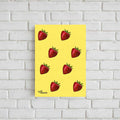 A vertical yellow art print featuring a pattern of red strawberries with green tops, displayed against a white brick wall. The print has the text 'Totally Trash Panda' printed in the bottom-left corner.