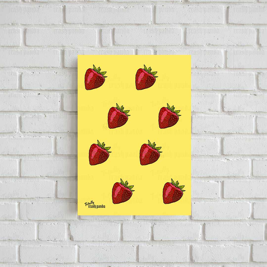 A vertical yellow art print featuring a pattern of red strawberries with green tops, displayed against a white brick wall. The print has the text 'Totally Trash Panda' printed in the bottom-left corner.